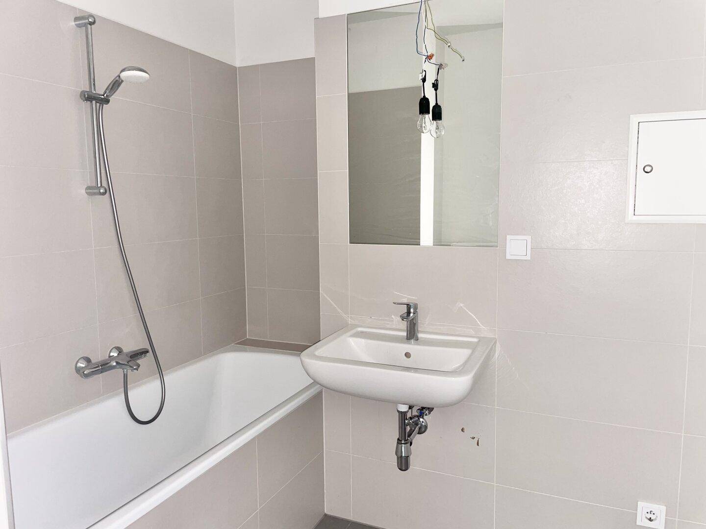 Modernes Badezimmer mit hellgrauen Fliesen, Badewanne mit Duschfunktion und Einzelwaschbecken.