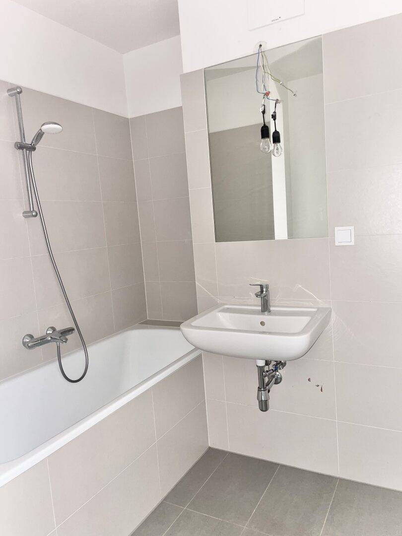 Helles Badezimmer mit Badewanne, Duscharmatur und einem Waschbecken mit großem Spiegel.