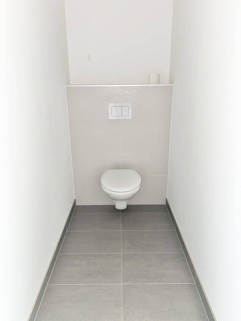 Separates WC mit wandhängender Toilette und modernen grauen Boden- und Wandfliesen.