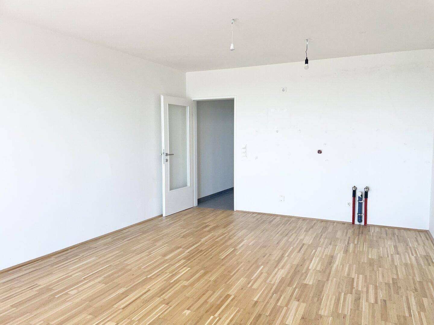 Leerer Raum mit Parkettboden und Anschlüssen für eine Küche, ideal für individuelle Küchenplanung.