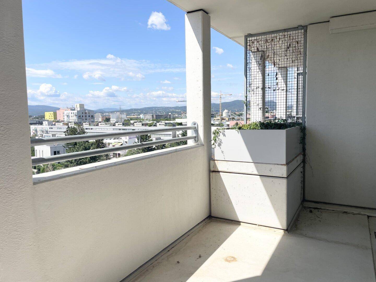 Balkon mit urbanem Ausblick über die Stadt und umliegende Gebäude an einem sonnigen Tag.