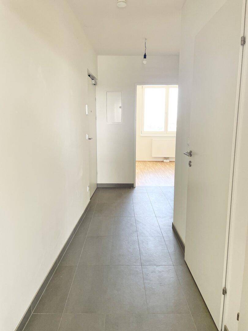 Heller Flur mit grauen Fliesen und Zugang zu weiteren Räumen mit Parkettboden.