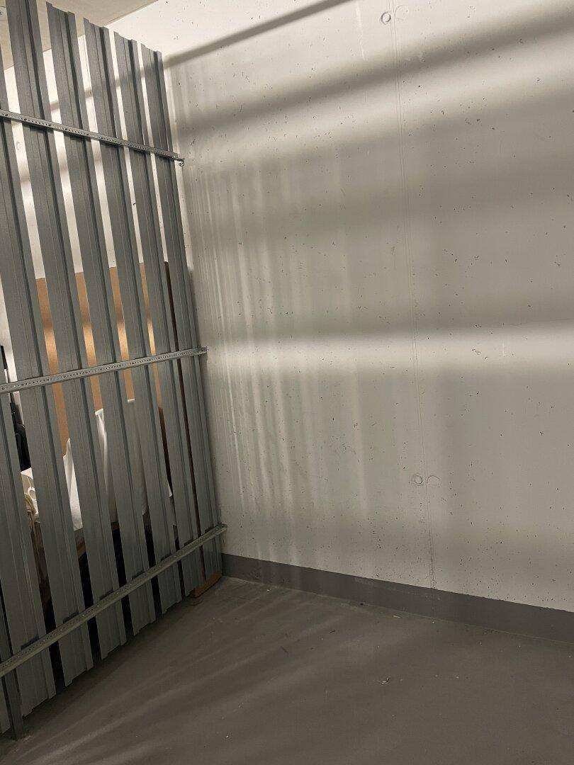 Einfacher Abstellraum mit Betonwänden und Metallabtrennung, ideal für zusätzlichen Stauraum.