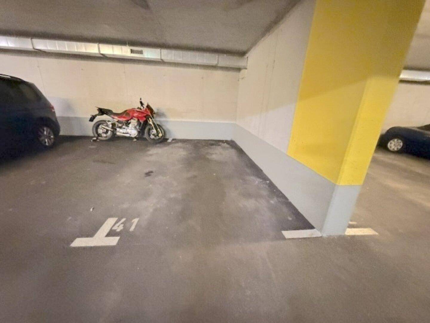 Tiefgaragenstellplatz mit Betonboden und gelbem Pfeiler, ein Motorrad parkt auf dem markierten Platz.