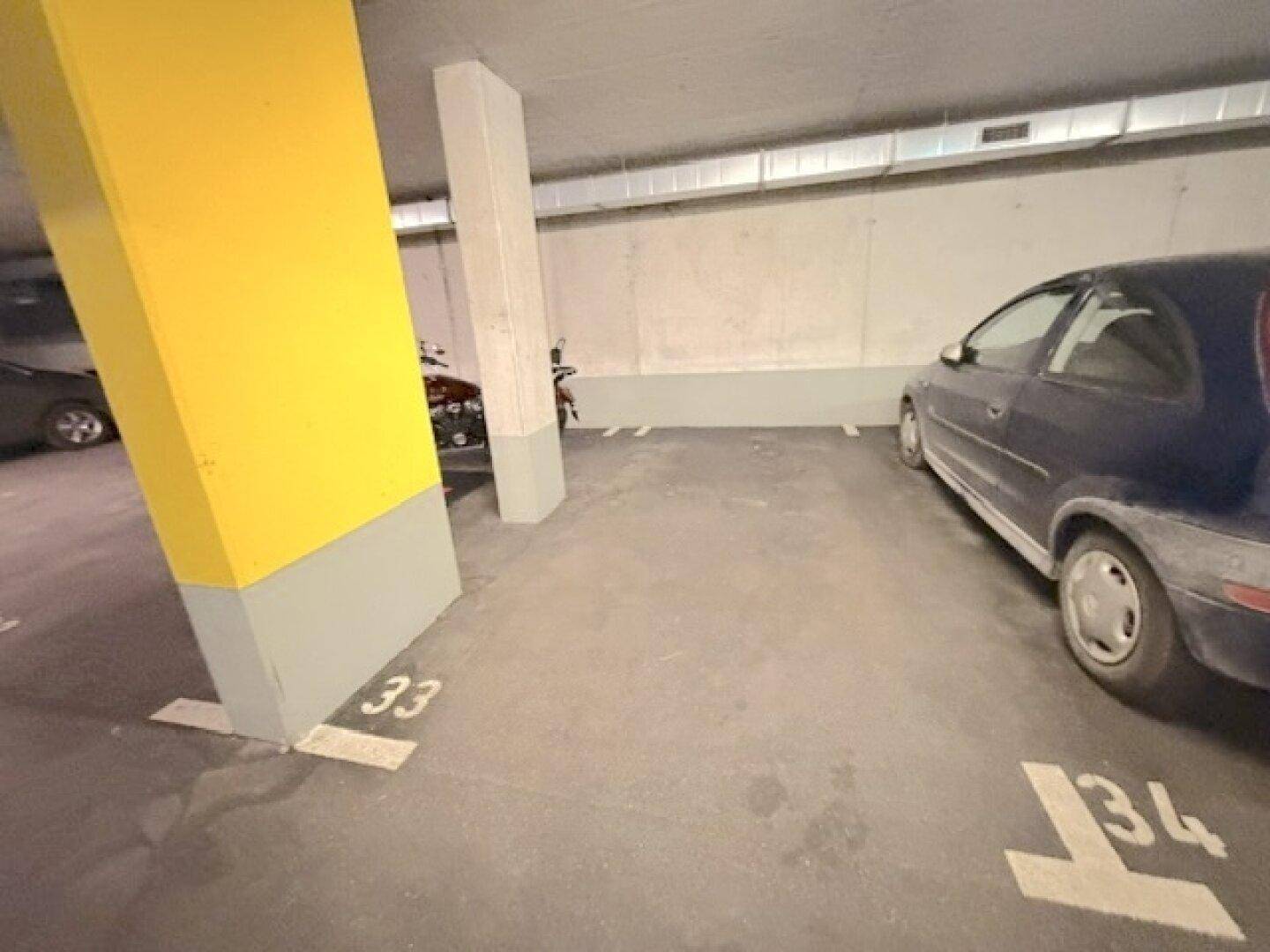 Tiefgaragenstellplatz mit Betonboden und gelbem Pfeiler, ein Kleinwagen parkt auf dem markierten Platz.
