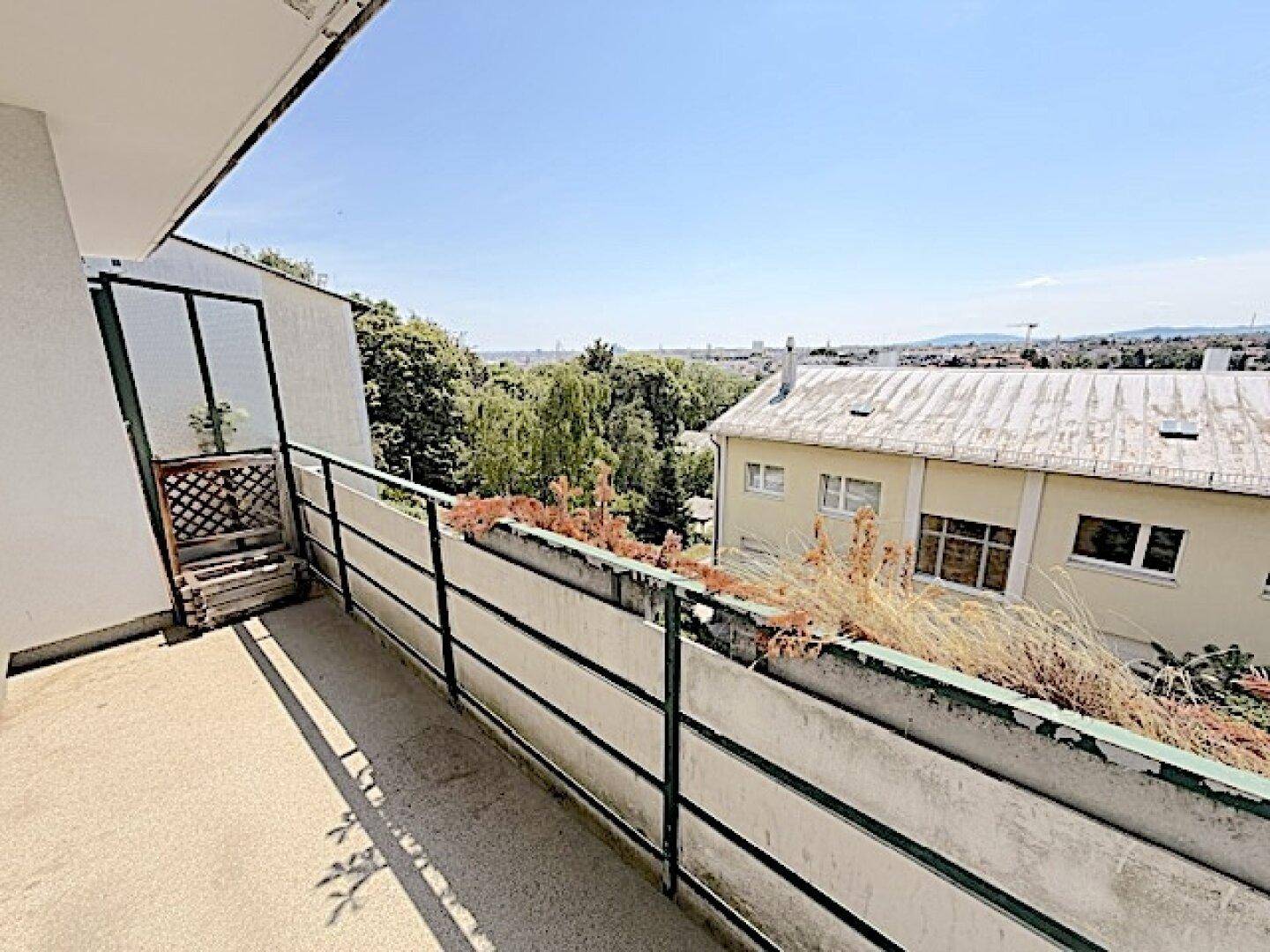 Langer Balkon mit Blick auf die umliegende Wohngegend und grüne Hügel.