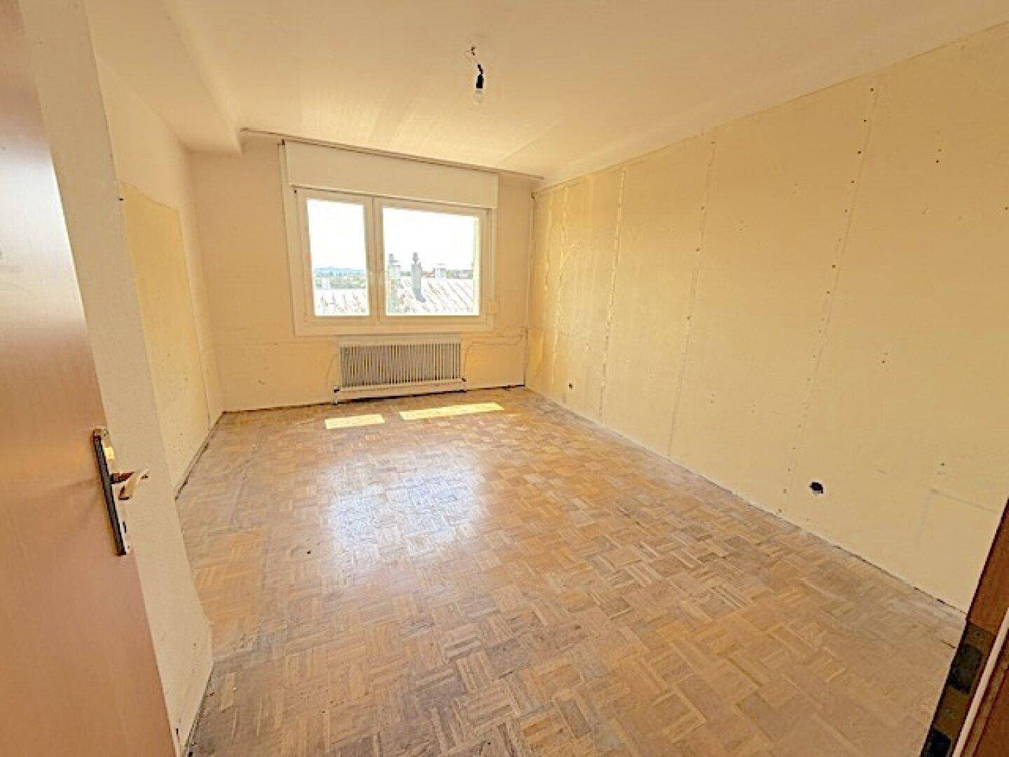 Helles Zimmer mit Parkettboden und Fenster mit Blick auf die Dächer.
