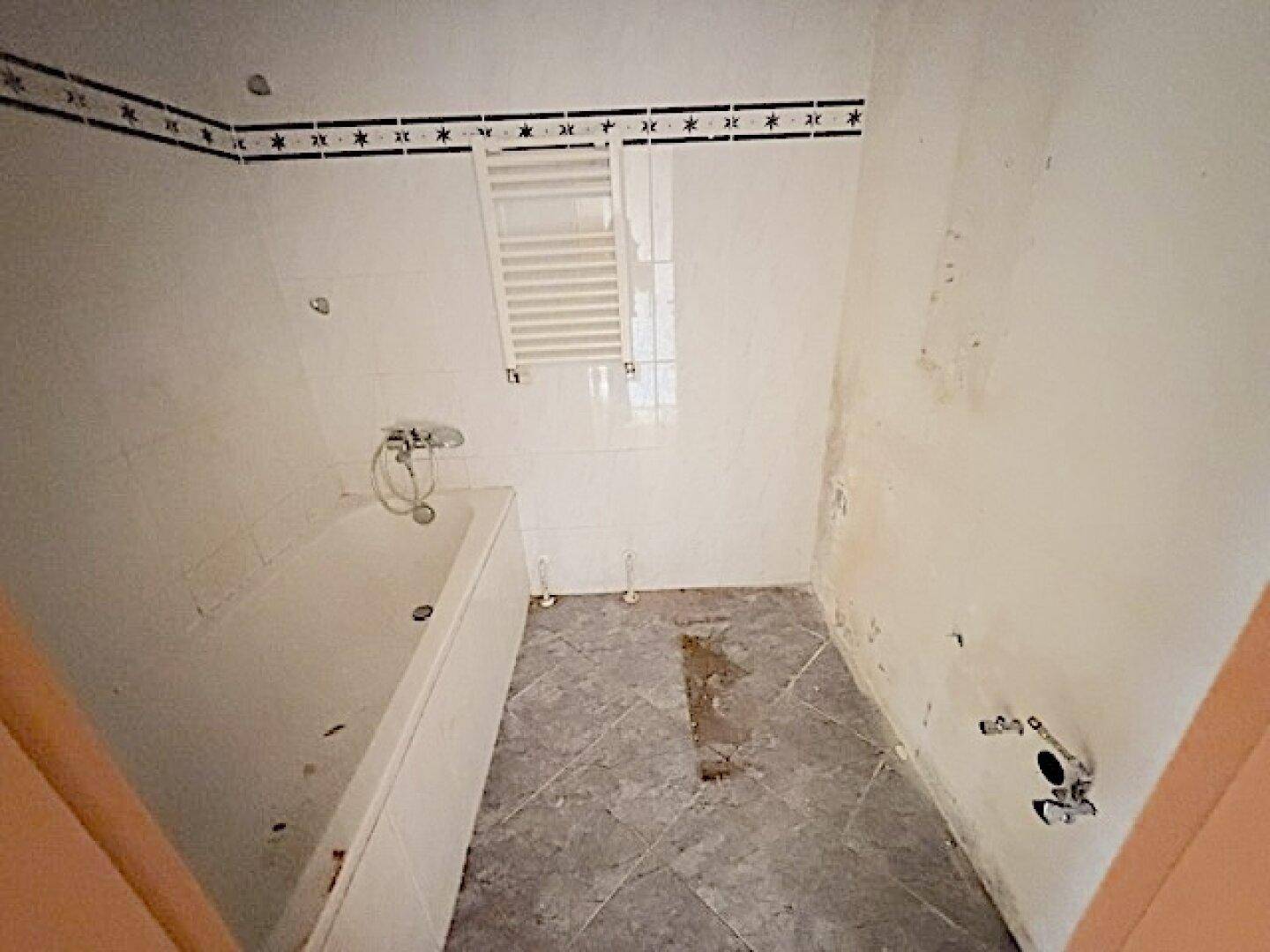 Badezimmer mit Badewanne, Fliesen und Heizkörper, renovierungsbedürftig.