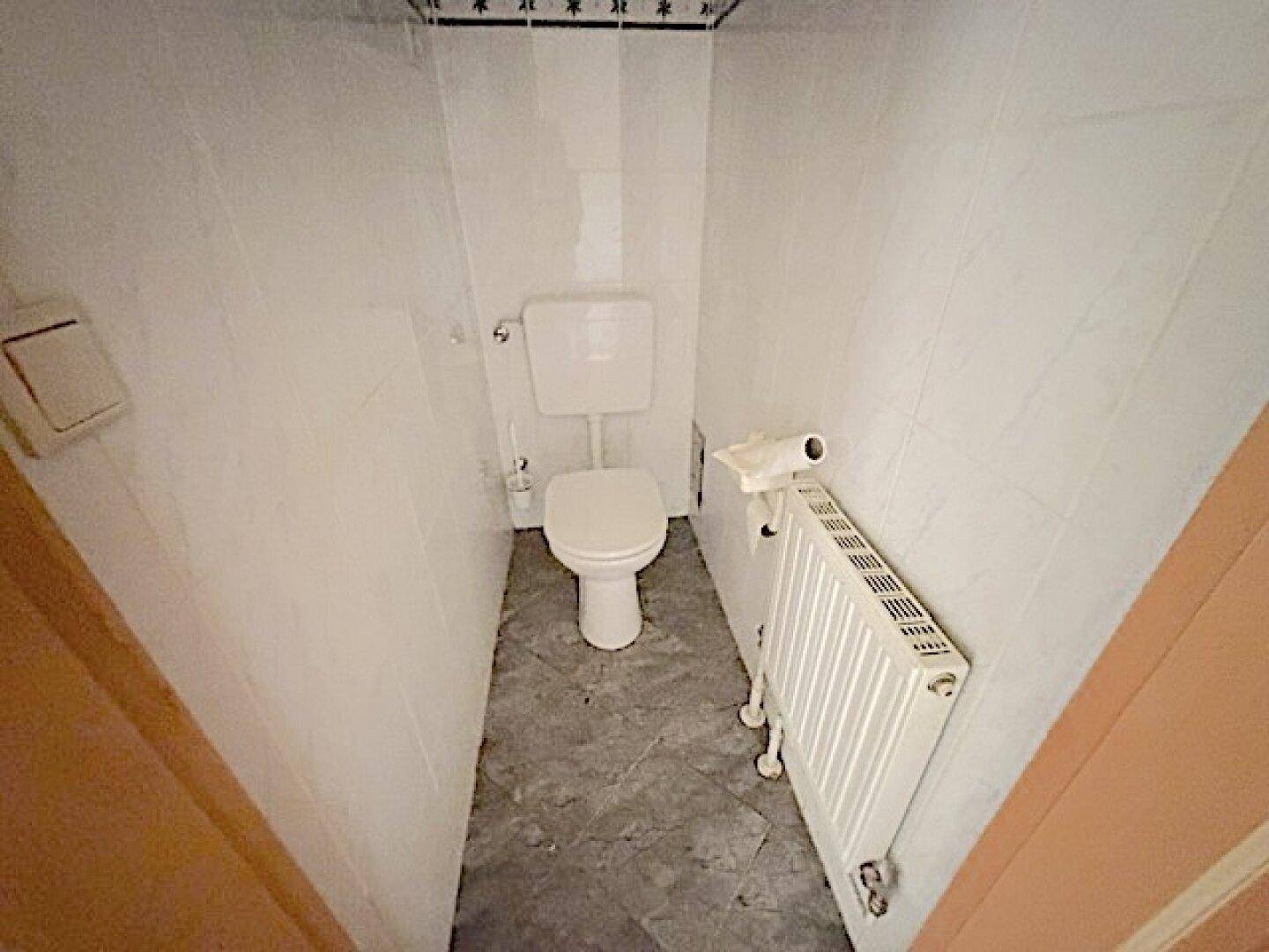 Separates WC mit Toilette, Fliesenboden und Heizkörper.