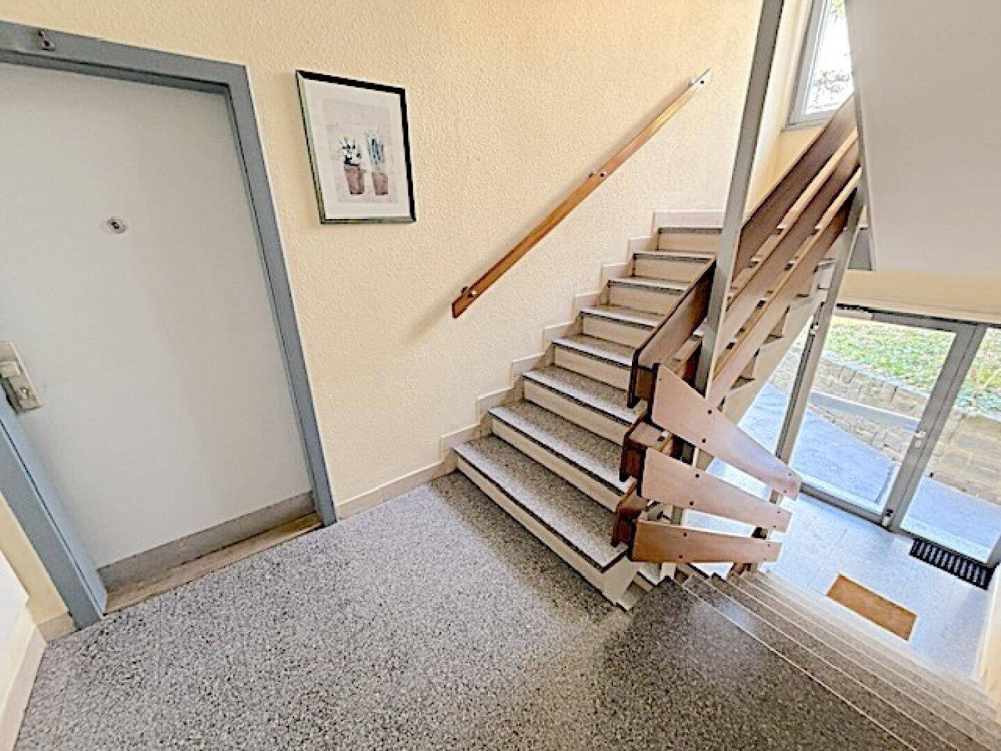 Treppenhaus mit Terrazzoboden und Holzgeländer in einem Mehrfamilienhaus.