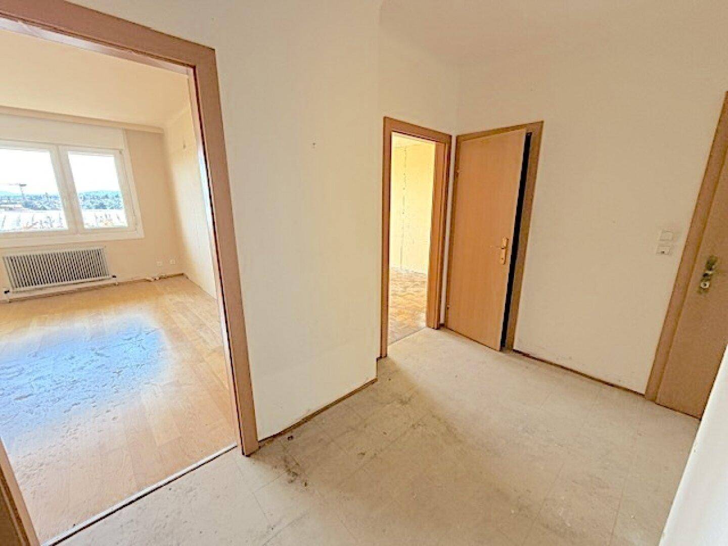 Heller Flur mit Zugang zu einem Zimmer mit Holzboden und Fenster.