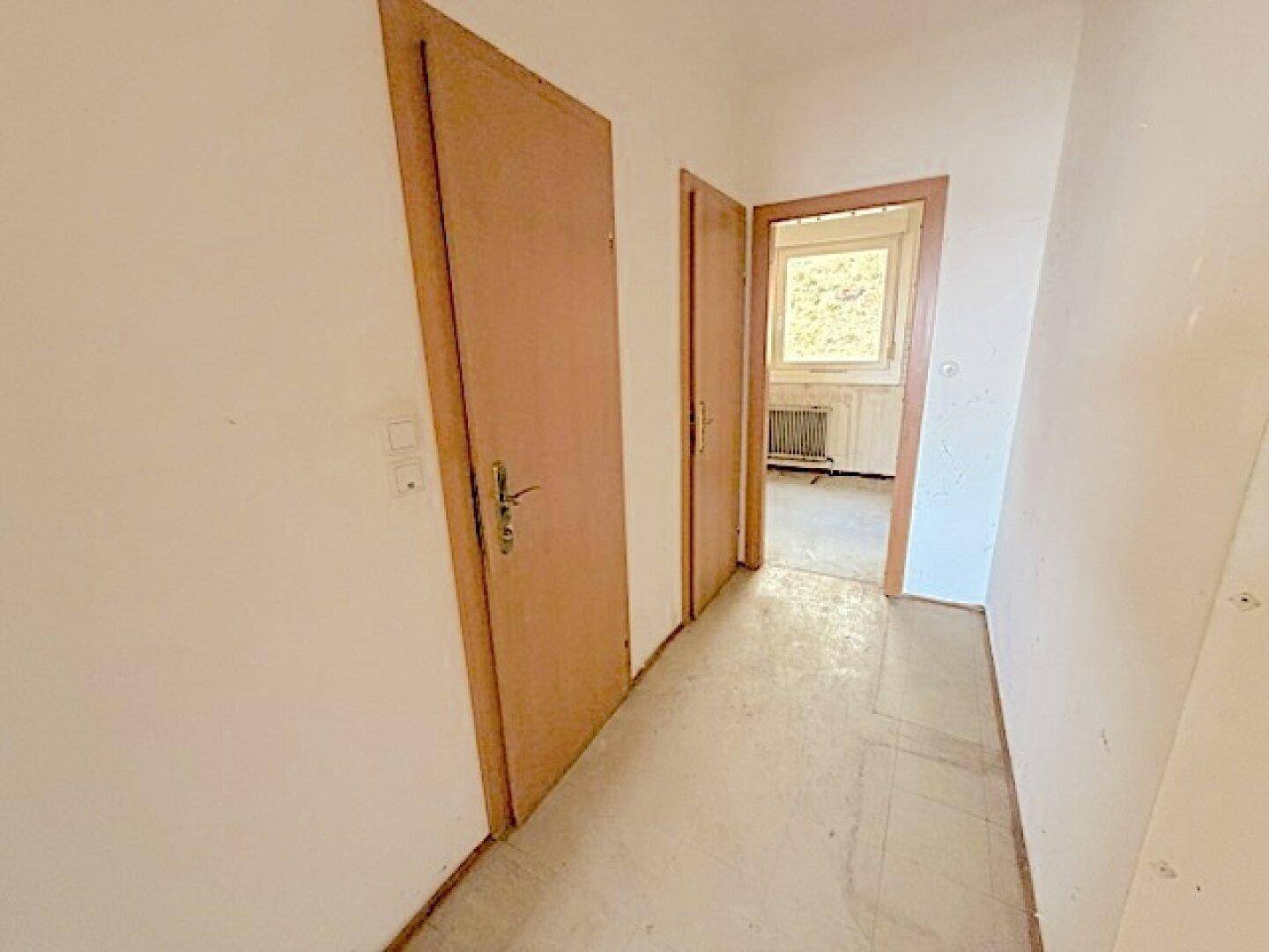 Langer Flur mit Türen zu verschiedenen Räumen und hellem Boden.