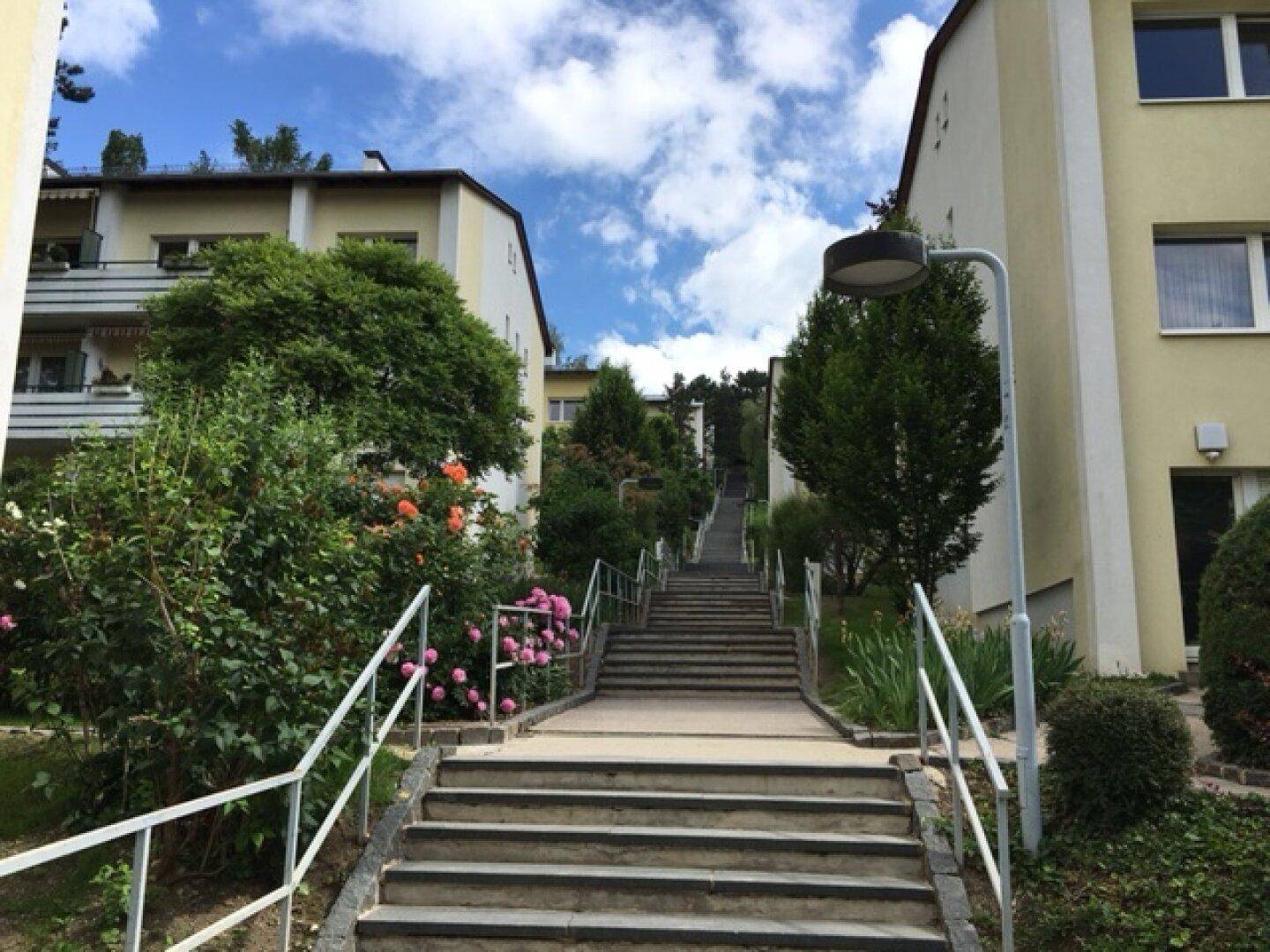Außenansicht eines Wohngebäudes mit Treppenaufgang und gepflegter Grünanlage.