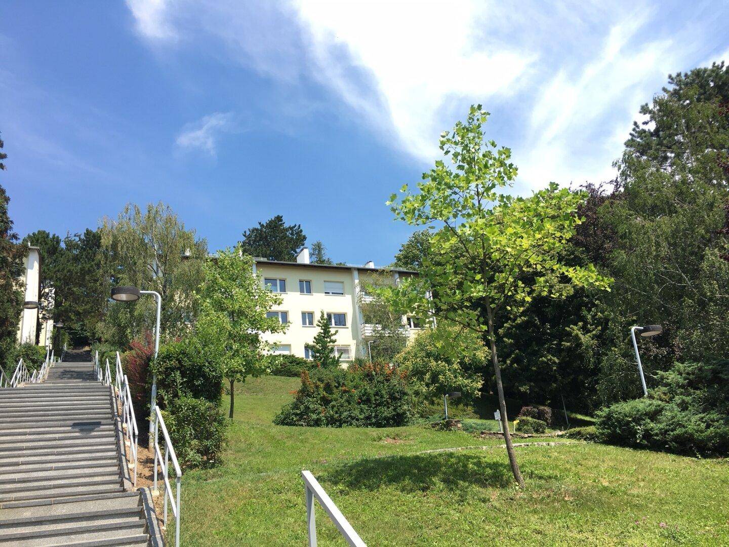 Wohngebäude in grüner Umgebung mit Bäumen und Sträuchern unter blauem Himmel.
