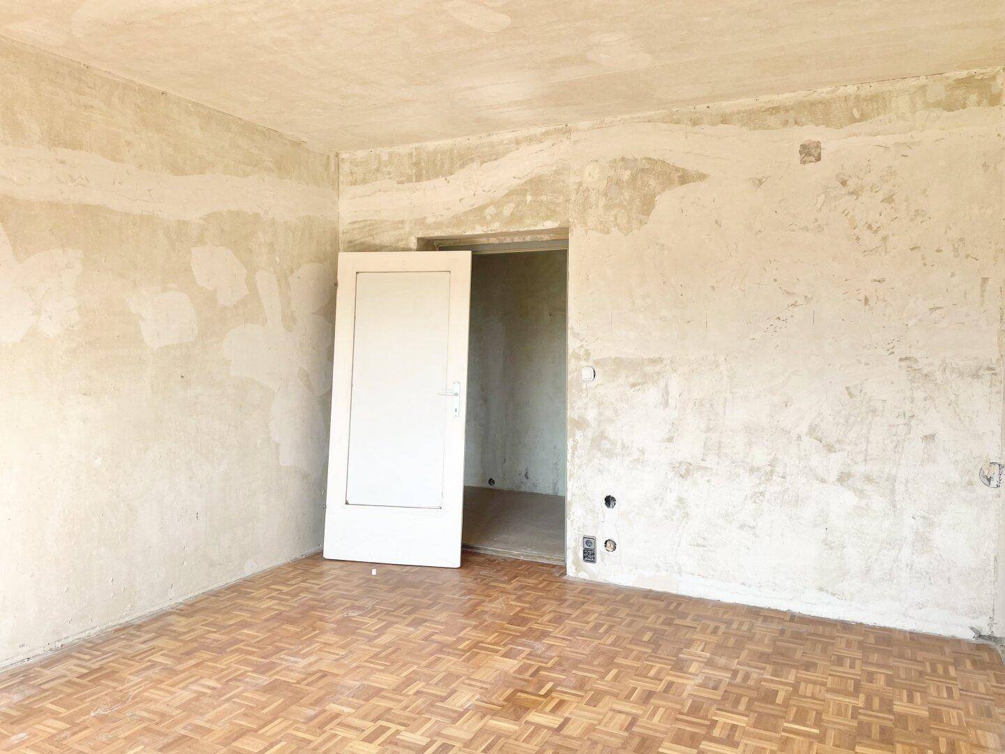 Leeres Zimmer mit Parkettboden und offener Tür, bietet Potenzial für individuelle Gestaltung.