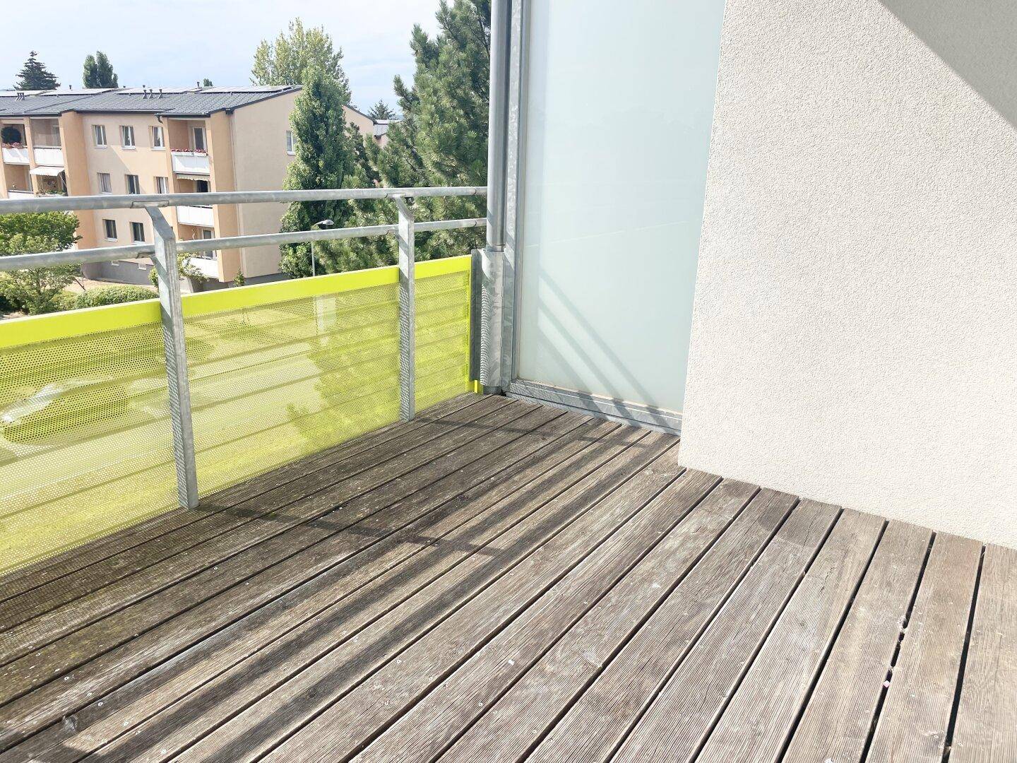 Geräumiger Balkon mit Holzdielen und modernem Sichtschutz aus Glas und Metall.