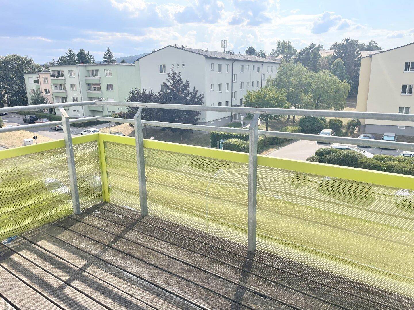 Balkon mit Holzboden und gelbem Sichtschutz, bietet einen Ausblick auf umliegende Gebäude.