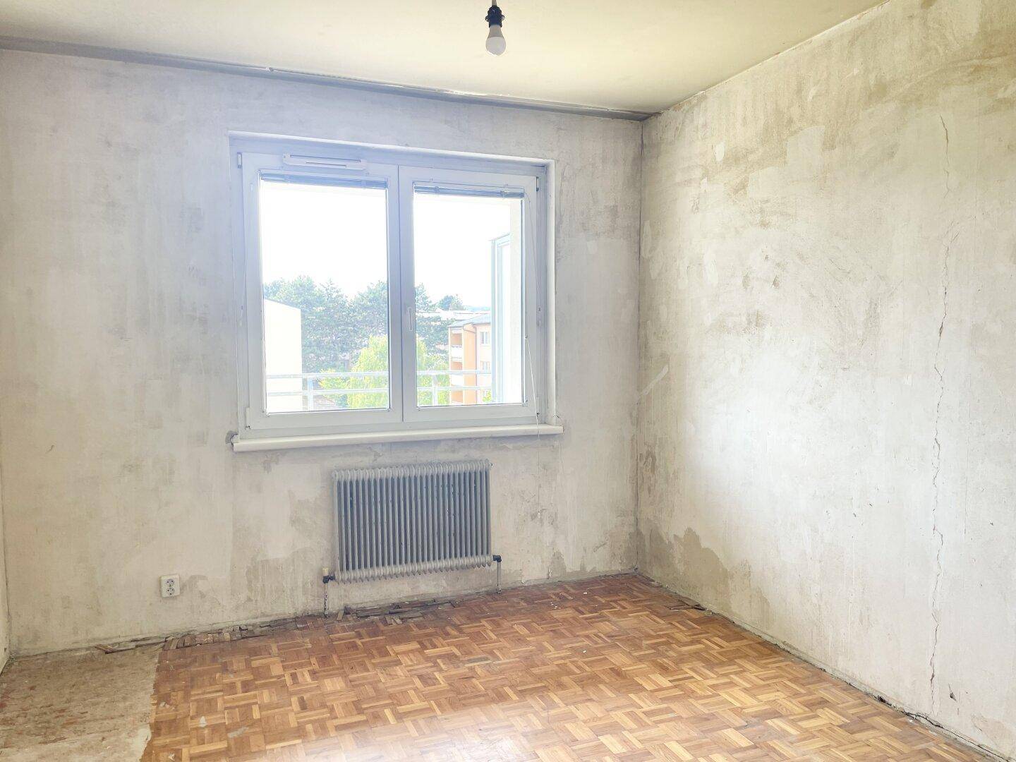 Helles Zimmer mit Parkettboden und Heizkörper, wartet auf die Fertigstellung und Einrichtung.