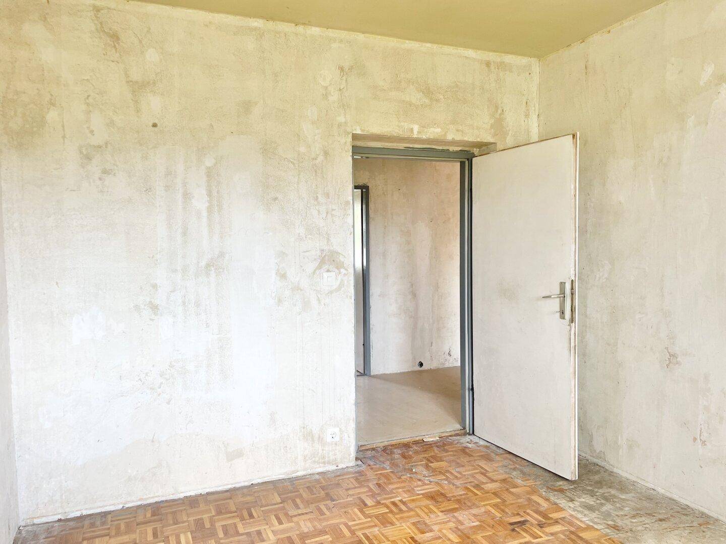 Unrenoviertes Zimmer mit Parkettboden und offener Tür, bereit für individuelle Renovierungsarbeiten.