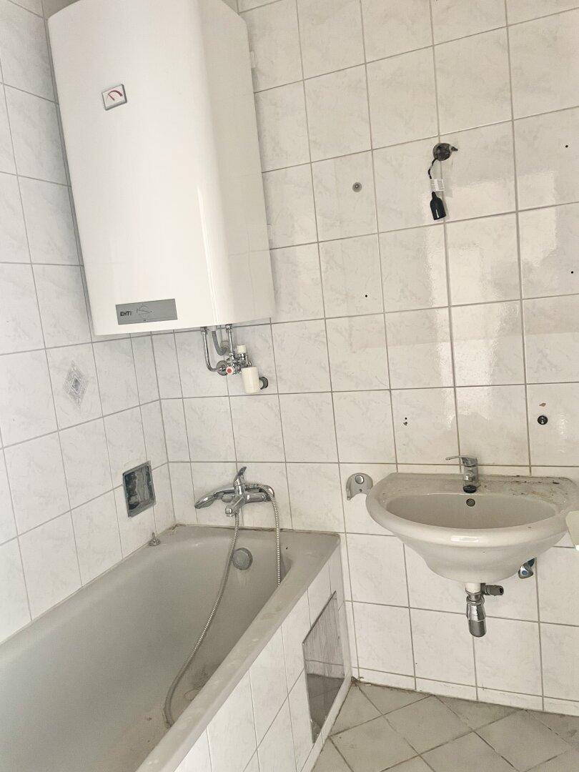Badezimmer mit Fliesen, Badewanne, Waschbecken und Warmwasserboiler, renovierungsbedürftig.