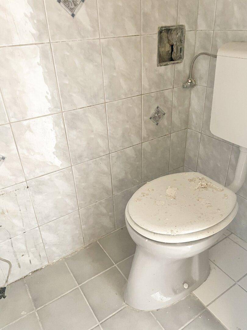 Separate Toilette mit hellen Fliesen an Wänden und Boden, in originalem Zustand.