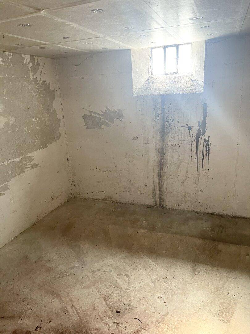 Kellerraum mit Betonwänden und kleinem Fenster, zeigt Spuren von Feuchtigkeit.