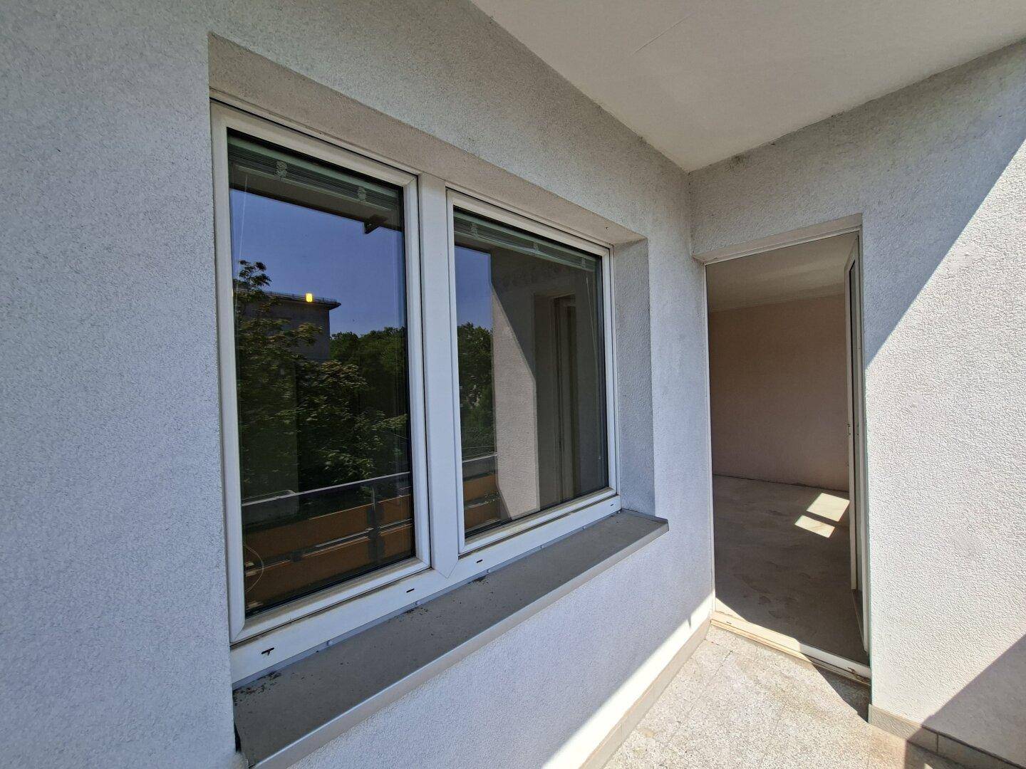 Heller Balkonbereich mit Fenster und Zugang zum Innenraum der Wohnung.