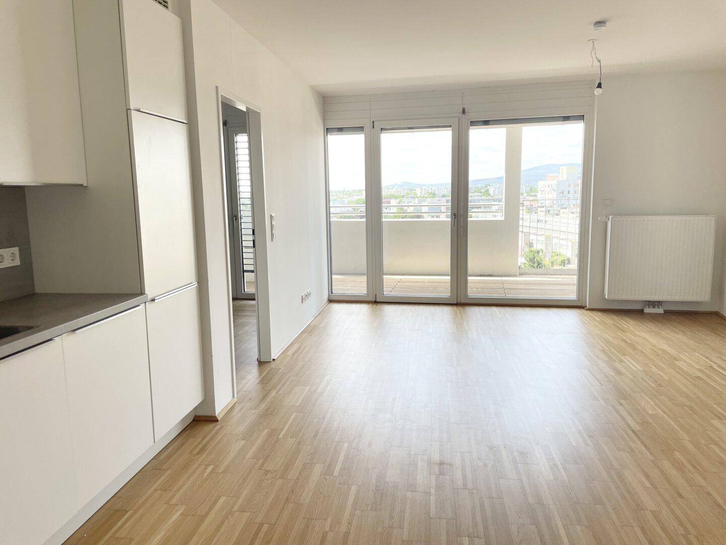 Helles Wohnzimmer mit Parkettboden und großen Fenstern, die Zugang zu einem Balkon bieten.