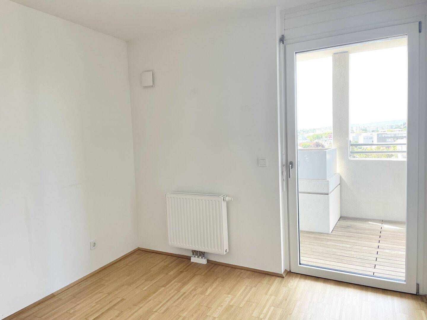 Helles Schlafzimmer mit Parkettboden und direktem Zugang zum Balkon durch eine große Glastür.