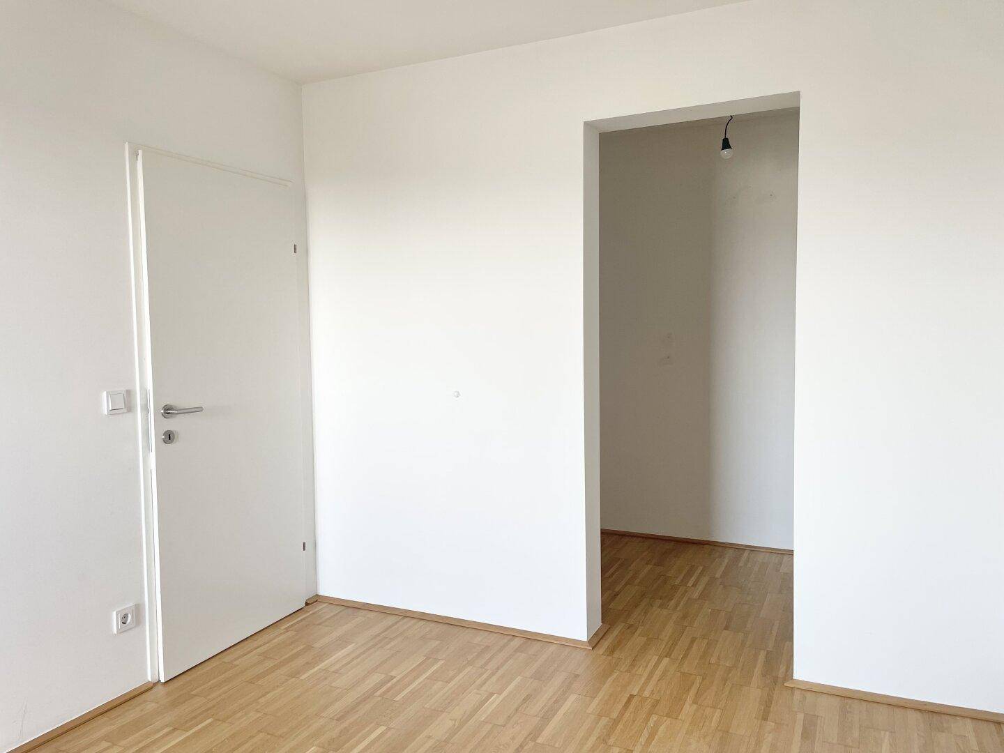 Leerer Raum mit hellem Parkettboden und weiß gestrichenen Wänden, bereit zur individuellen Gestaltung.