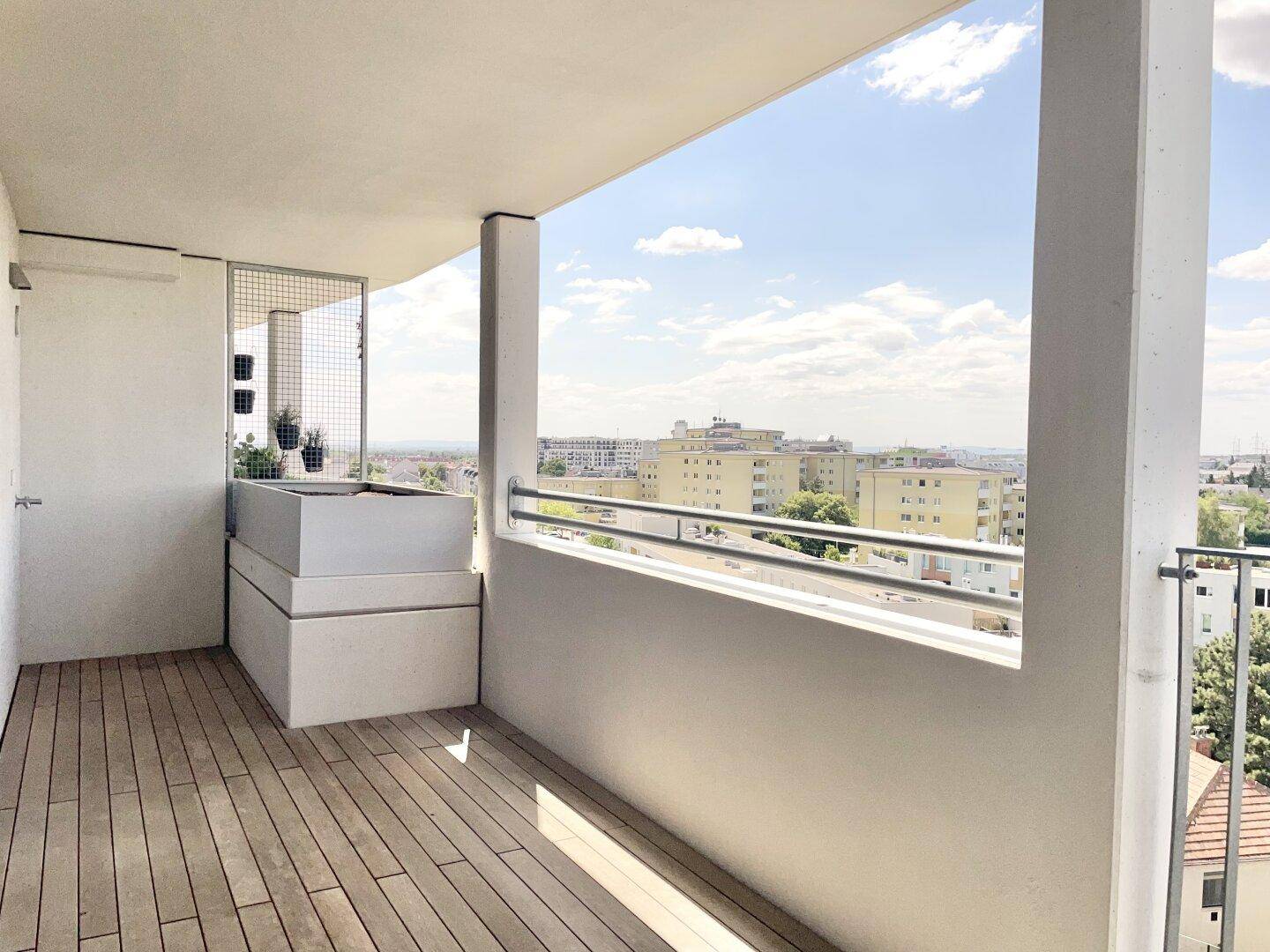 Heller Balkon mit Holzdielen und einem modernen Pflanzgefäß, bietet einen weiten Stadtblick.