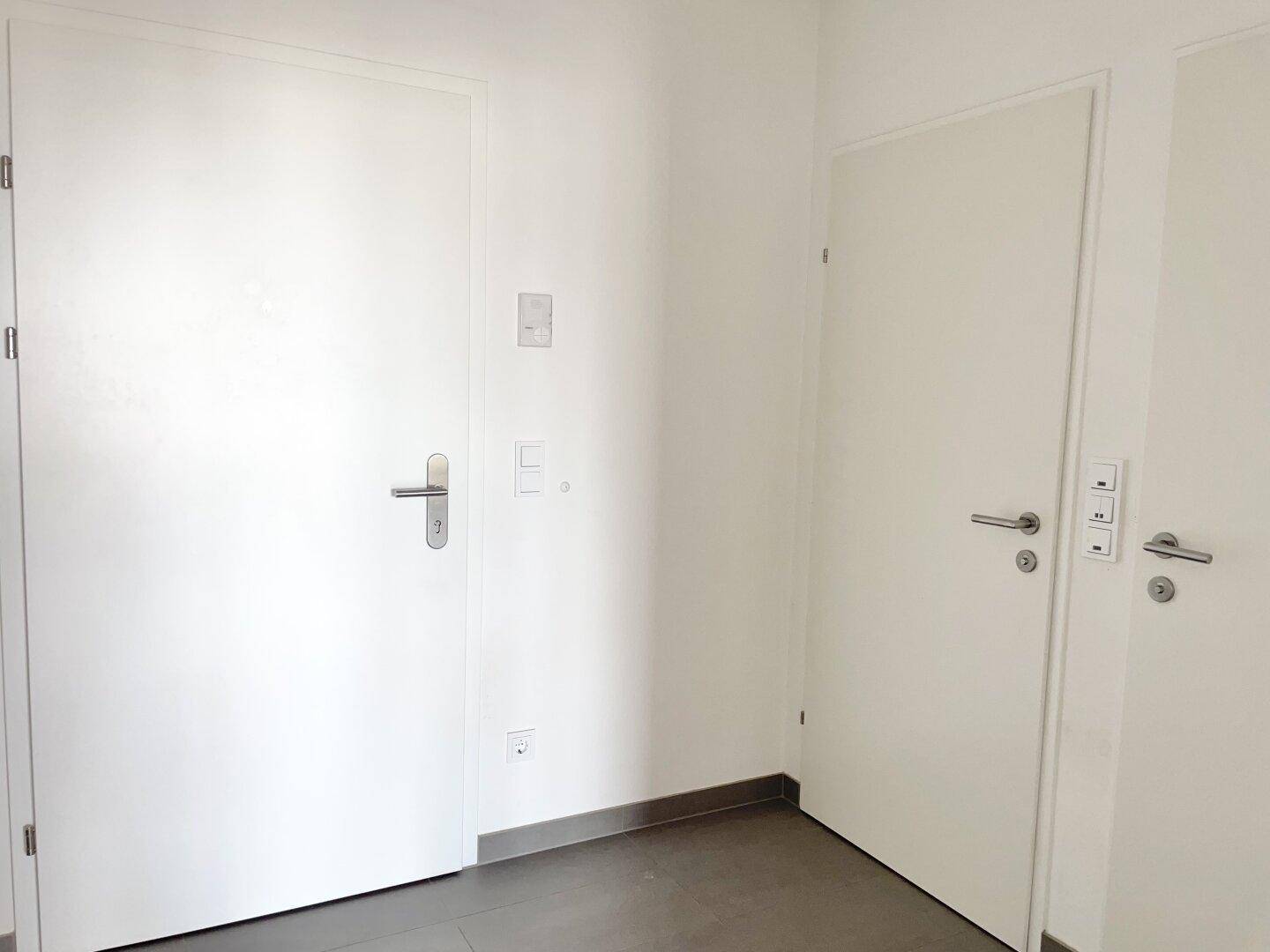 Heller Flurbereich mit zwei weißen Türen und modernen grauen Bodenfliesen.