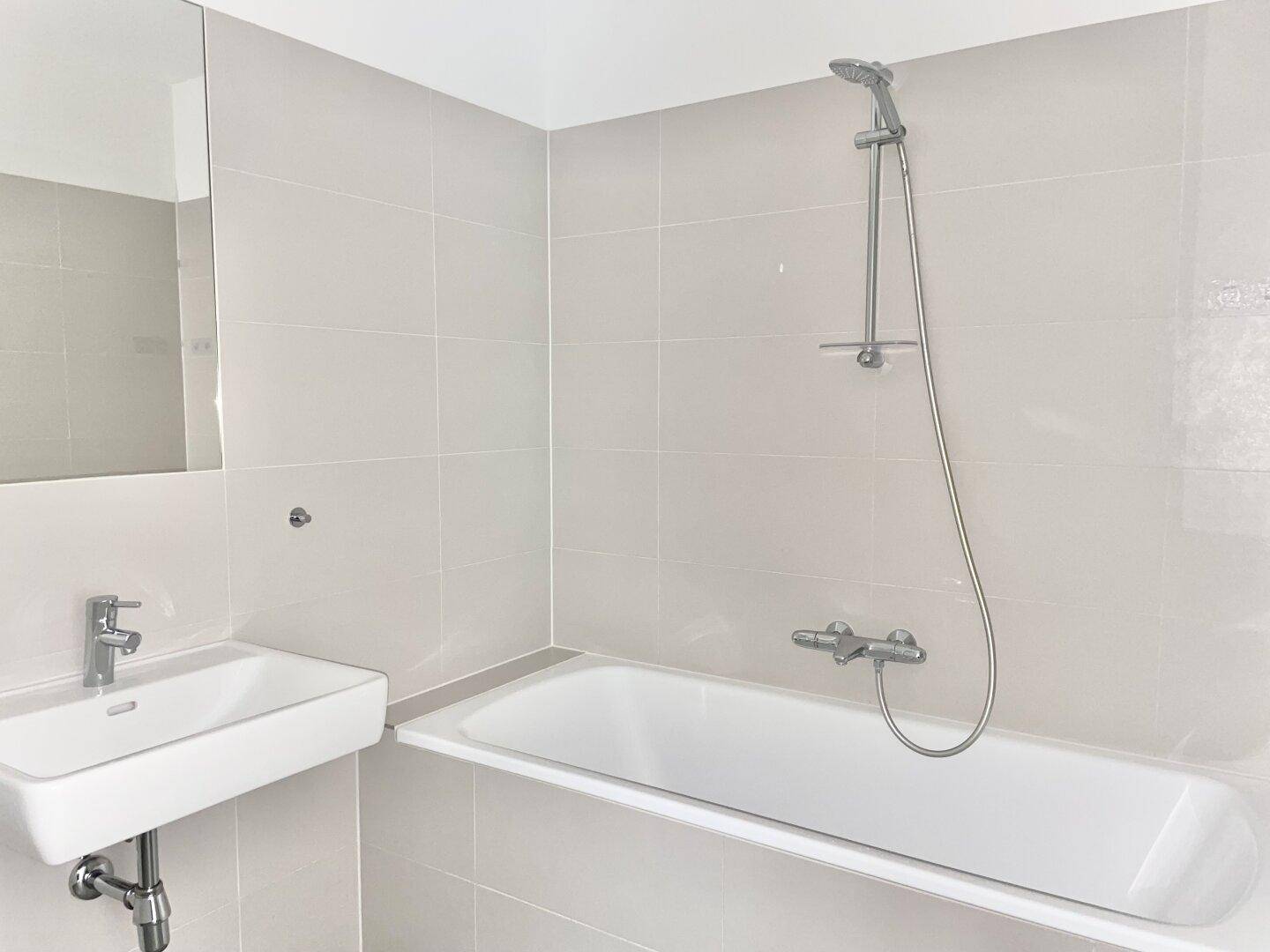 Detailansicht des Badezimmers mit Badewanne, Duscharmatur und modernem Waschbecken.