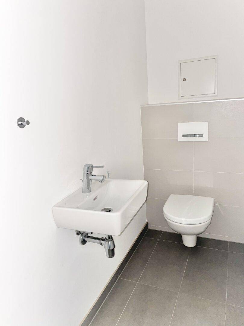 Separates Gäste-WC mit wandhängender Toilette und kleinem Handwaschbecken.