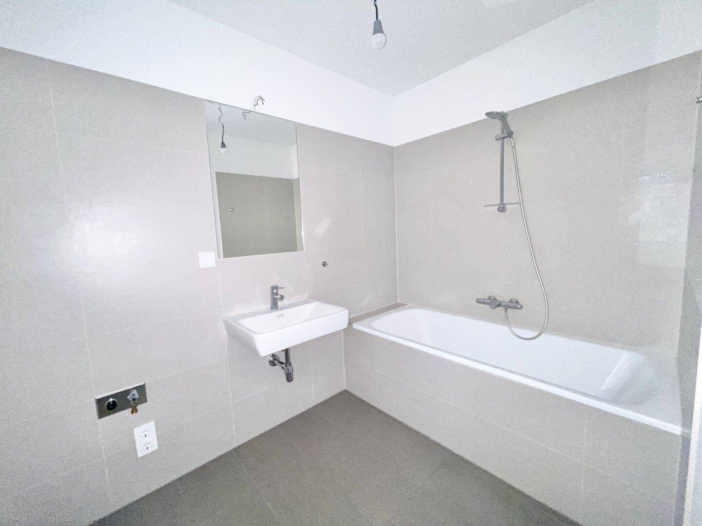 Modernes Badezimmer mit hellgrauen Fliesen, Badewanne mit Duschfunktion und Einzelwaschbecken.