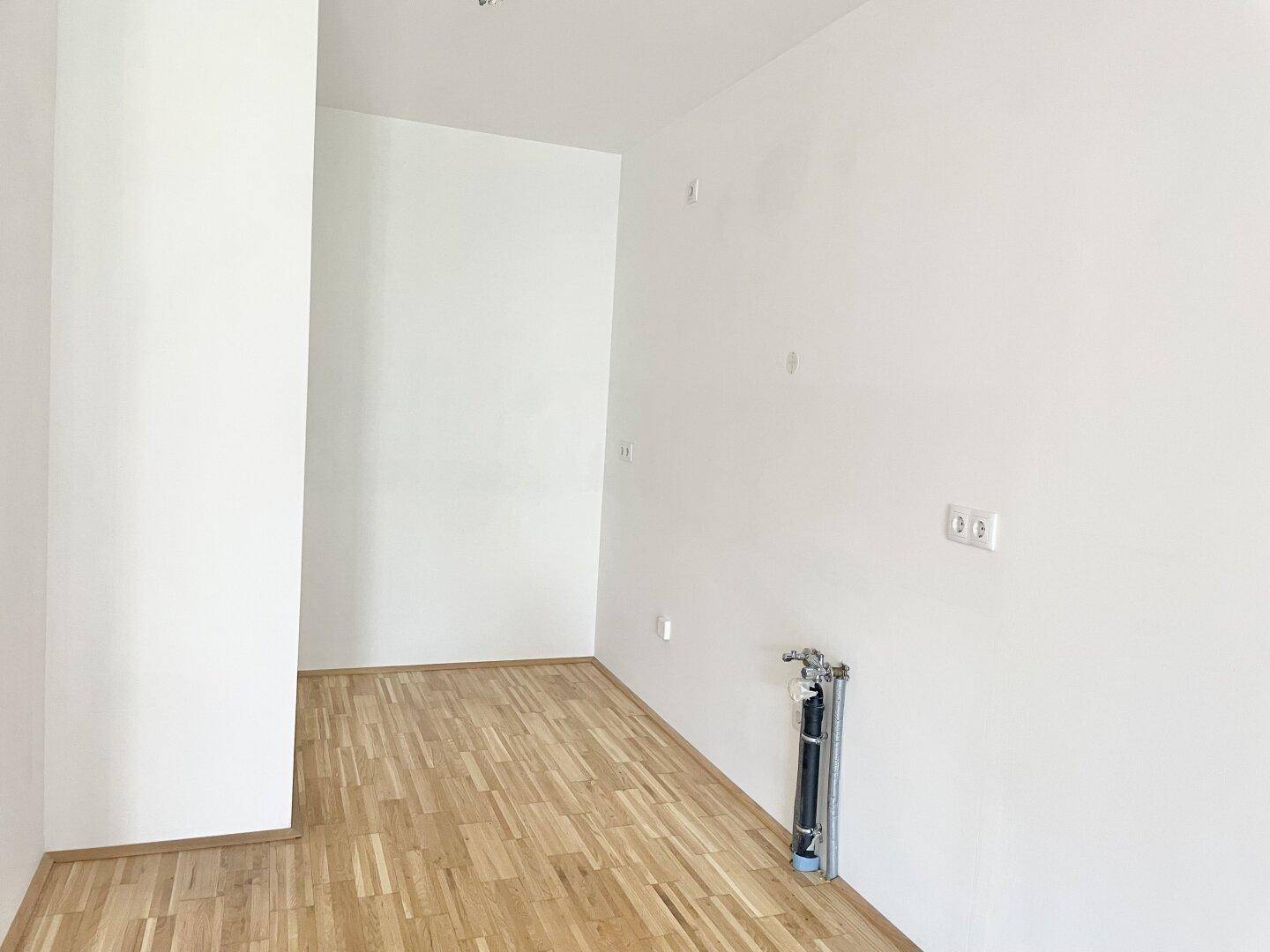 Leerer Raum mit Holzboden und sichtbaren Anschlüssen, ideal für eine Küche oder einen Hauswirtschaftsraum.