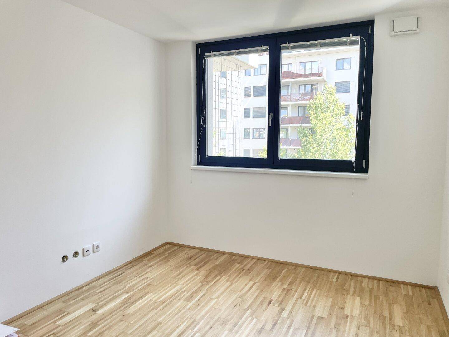 Helles Schlafzimmer mit Holzboden und einem Fenster, das den Blick nach draußen freigibt.