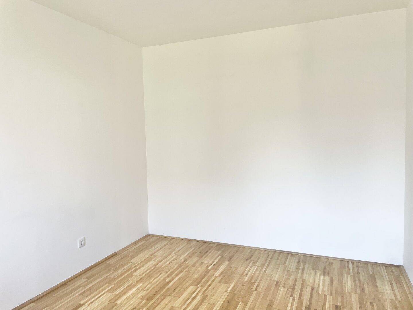 Leerer, heller Raum mit Holzboden und weißen Wänden, bereit zur individuellen Gestaltung.