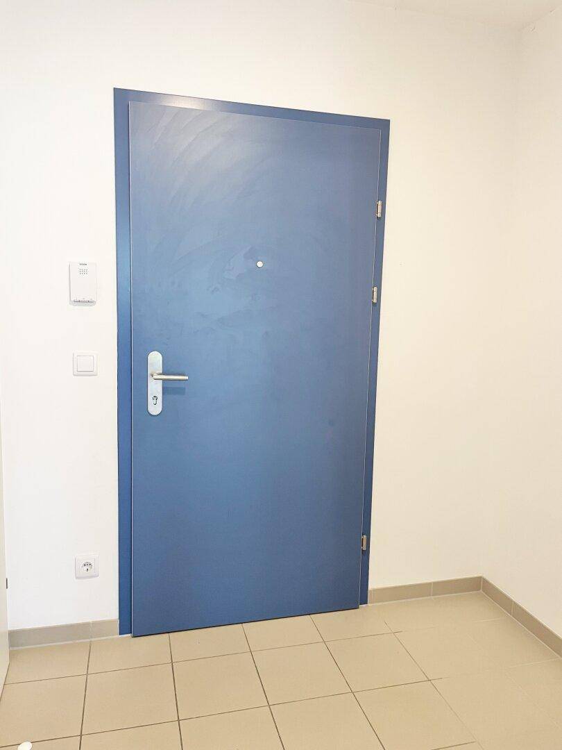 Eingangstür in kräftigem Blau, die zu einem gefliesten Flur führt.