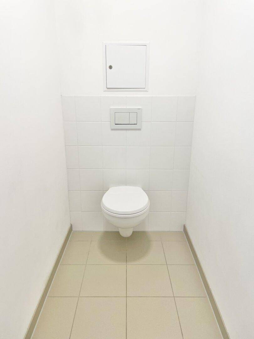 Separates WC mit wandhängender Toilette und hellen Fliesen an Wänden und Boden.