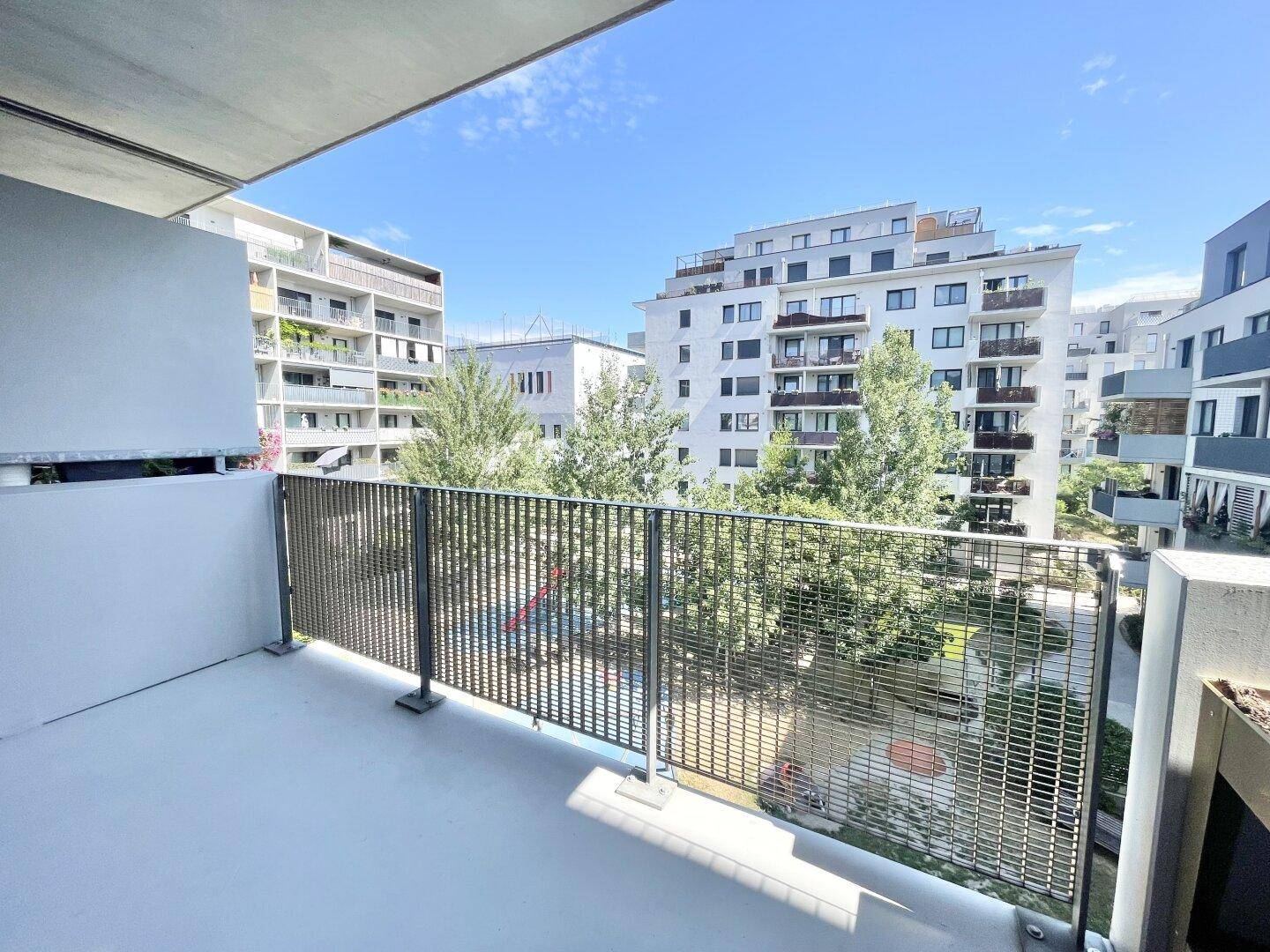Balkon mit Blick auf einen Spielplatz und moderne Wohngebäude unter blauem Himmel.