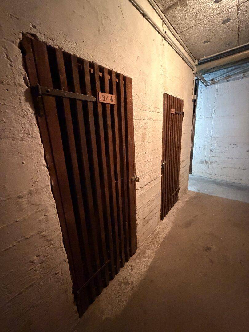 Kellerabteil mit Holztüren und Betonwänden in einem älteren Gebäude, ideal als Stauraum.