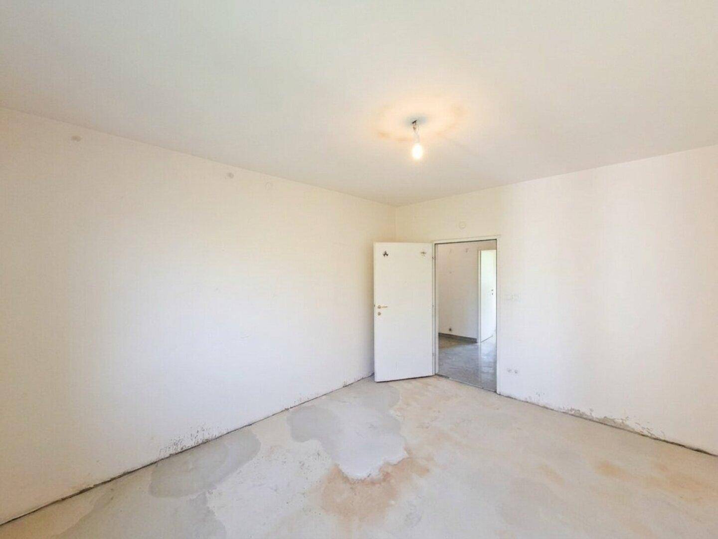 Geräumiges, unmöbliertes Zimmer mit weißen Wänden und offener Tür.