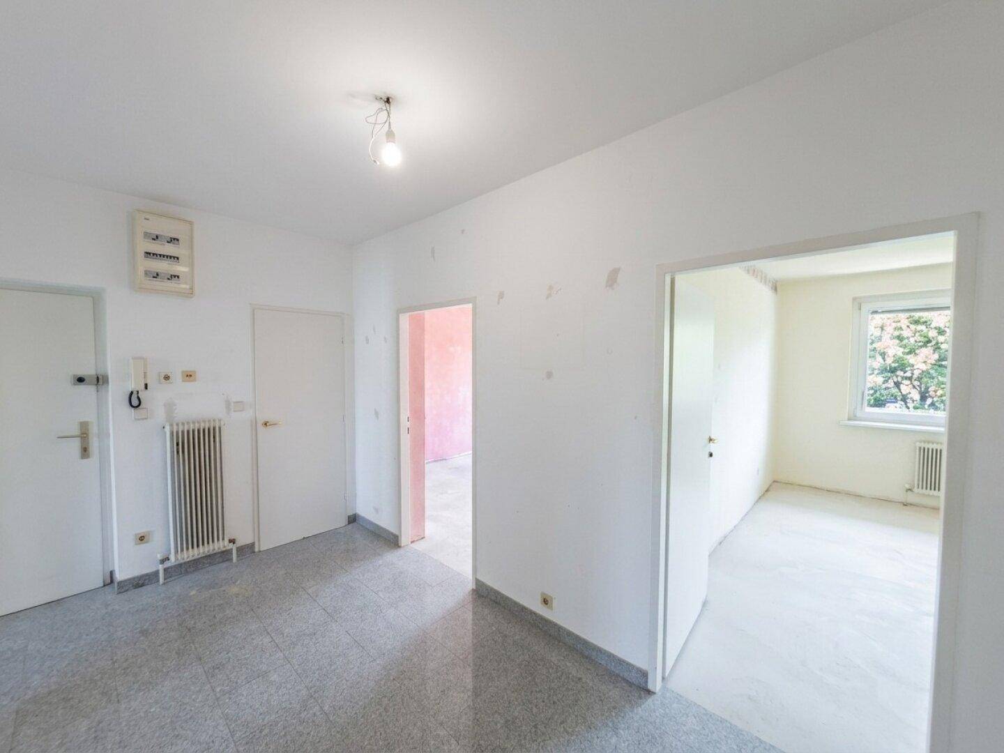 Heller Flur mit grauem Fliesenboden, Heizkörper und mehreren Türen zu den Zimmern.