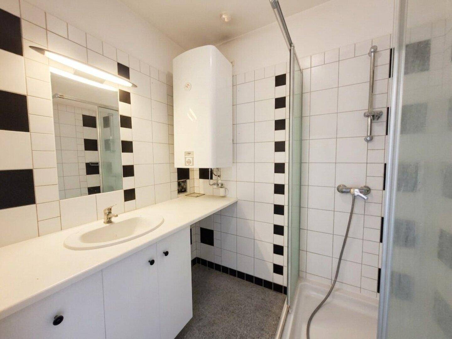 Badezimmer mit schwarz-weißen Fliesen, Einzelwaschbecken, Duschkabine und Warmwasserboiler.
