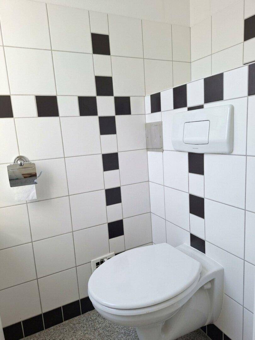 WC-Bereich mit schwarz-weißen Fliesen und wandhängender Toilette.