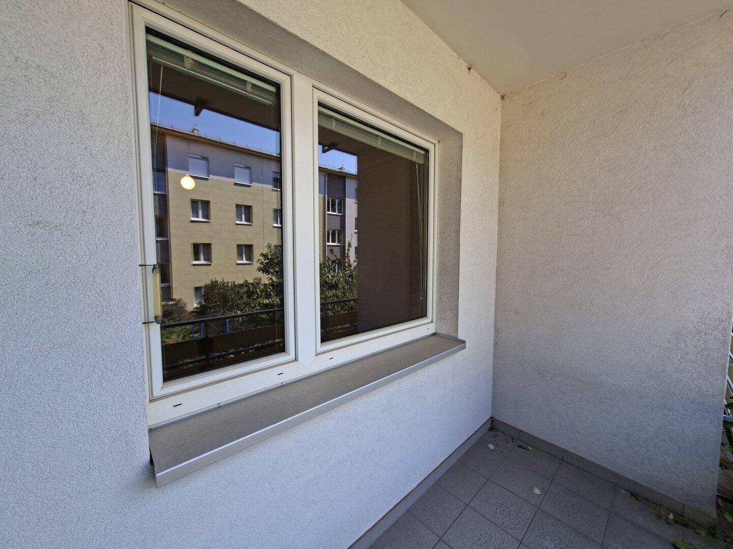 Kleiner Balkonbereich mit Fliesenboden und Fenster, das den Blick auf die Umgebung reflektiert.