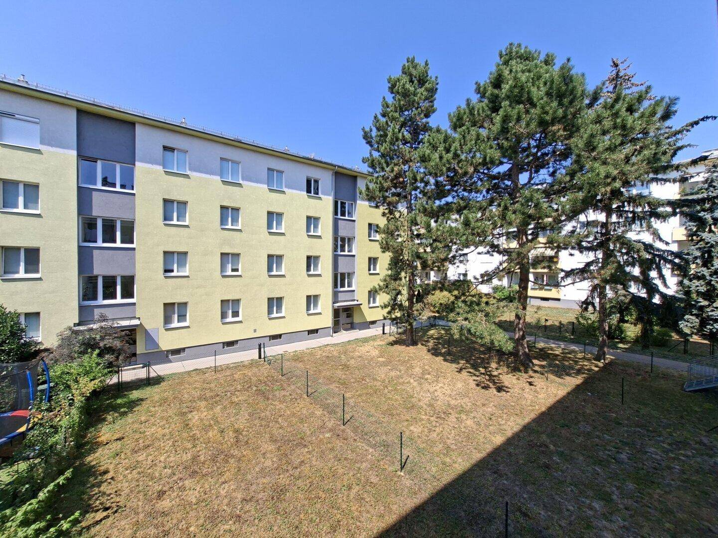 Außenansicht eines Mehrfamilienhauses mit gelb-grauer Fassade und Bäumen im Vordergrund.