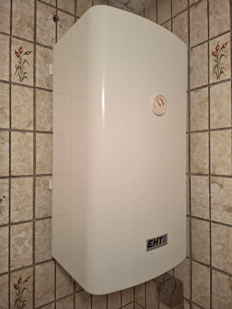 Detailansicht eines Warmwasserboilers an einer gefliesten Wand im Badezimmer.