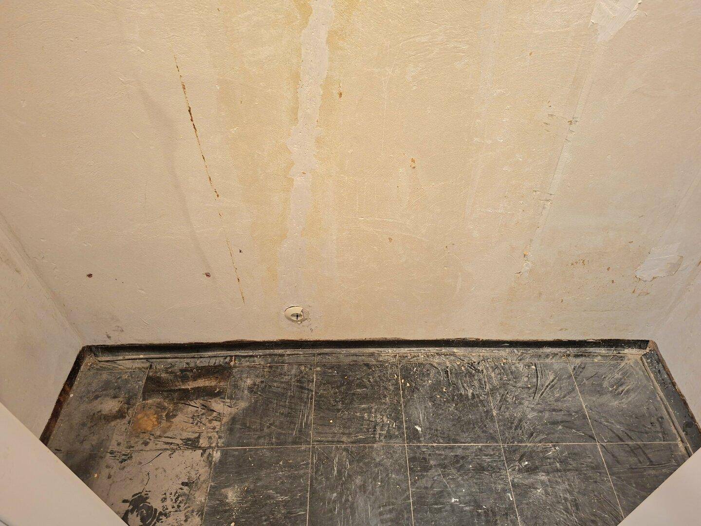 Kleiner Raum mit dunklem Fliesenboden und Spuren von Renovierungsarbeiten an der Decke.